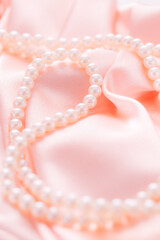 Pearl necklace on pink satin fabric. Soft focus