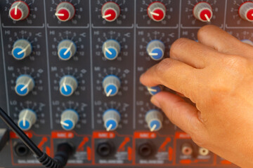 Technician's hand tuning adjustment on audio control panel in booth at the audio system equipment...