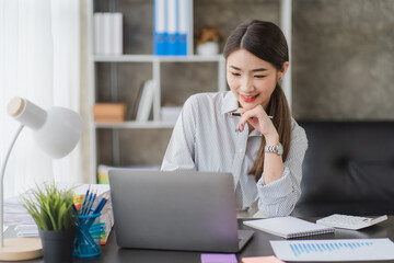 Portrait of smiling happy beautiful Asian woman relaxing using technology of laptop computer while sitting on table.Young creative girl working and typing on keyboard at cafe.work at home concept