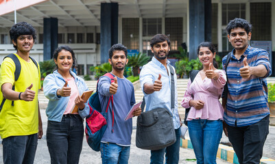 Confident students with backpack and books showing thumbs up by looking camera at college campus - concept of approval, education and development.