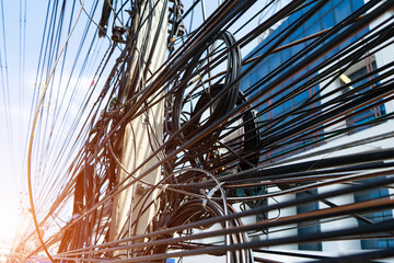 Electric wire or power cable are tied up in a disorderly manner with sunlight background. Which may...