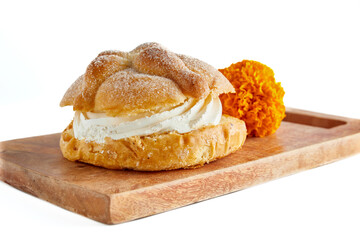 Celebración de día de muertos en México con pan de muerto relleno de crema pastelera sobre tabla de madera y en fondo blanco