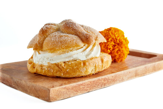 Celebraci&oacute;n de d&iacute;a de muertos en M&eacute;xico con pan de muerto relleno de crema pastelera sobre tabla de madera y en fondo blanco