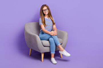 Full length photo of adorable intelligent girl wear striped t-shirt sit in armchair hands on knee isolated on purple color background