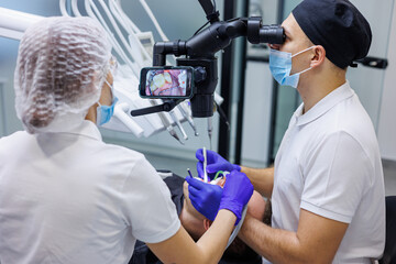 A dentist and an assistant treat a patient's teeth using a microscope. Professional teeth cleaning. Dental office. Dental microscope.