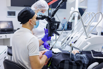 A dentist and an assistant treat a patient's teeth using a microscope. Professional teeth cleaning. Dental office. Dental microscope.