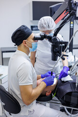 A dentist and an assistant treat a patient's teeth using a microscope. Professional teeth cleaning. Dental office. Dental microscope.