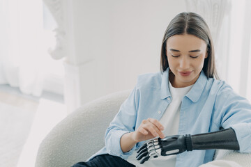 Young pretty disabled girl customizing bionic prosthesis of arm, touching robotic prosthetic hand