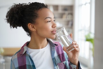 Mixed race young girl drink pure water from glass at home. Healthy lifestyle, morning routine