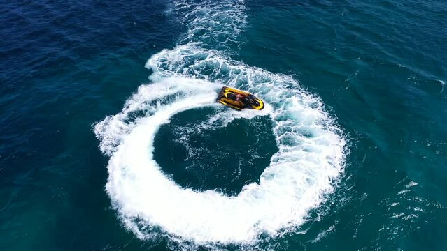 Aerial drone top down video of jet ski watercraft performing circles showing off in high speed operated by stuntman in deep blue sea