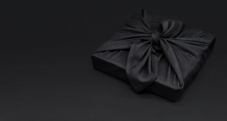 Black friday gift box wrapped in fabric with copy space. Traditional Japanese gift wrapping furoshiki style. Eco friendly holiday concept.