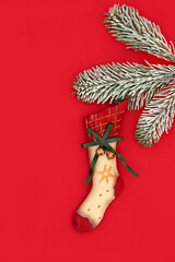 Retro Christmas stocking tree vintage metal ornament decoration hanging from snow covered fir branch on red background. Old fashioned symbol of Xmas Eve.