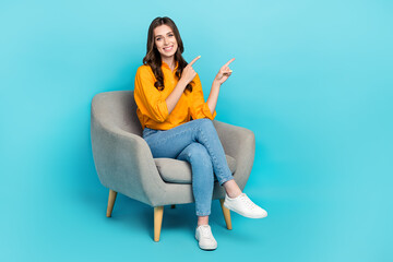 Full size portrait of cheerful nice girl sit chair indicate fingers empty space isolated on blue color background