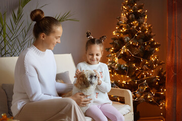 Photo of woman with bun hairstyle wearing white sweater sitting with her little daughter and...