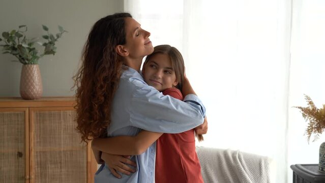 Friendly European woman with daughter at moment of congratulations on holiday or birthday stand in home interior. Happy teenage girl hugging mother after long separation or leaving for children's camp