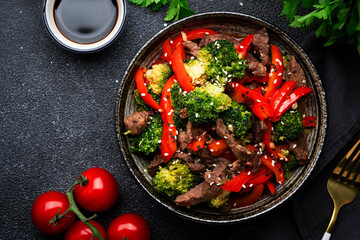 Stir fry vegetables with beef, paprika and broccoli with sesame seeds in bowl on black table  background, top view
