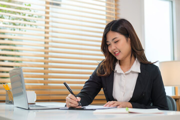 Charming young woman sitting in bright home office and using laptop computer.