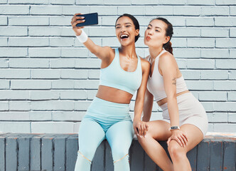 Fototapeta na wymiar Fitness friends, phone selfie and picture for social media, influencer content and happy workout after exercise and training by brick wall. Fit females take wellness, fun and online motivation photo