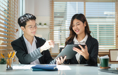 Two young business colleagues discussing financial data, working together in bright workplace.