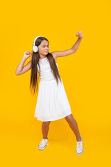 teen girl listen music in headphones and dancing on yellow background