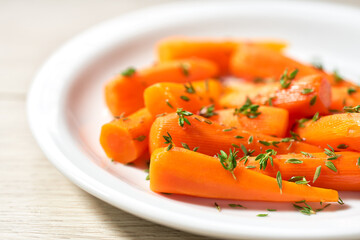 Baked (roasted) honey glazed baby carrots with thyme on a white ceramic plate, close-up.