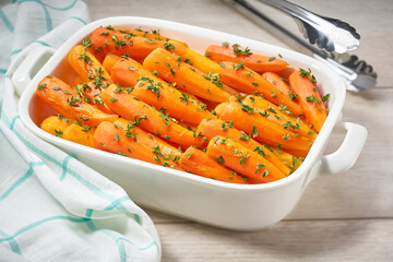 Fried baby carrots with fresh thyme in a ceramic form on a wooden table. Caramelized Carrots. A healthy carrot dish that is rich of vitamin A.