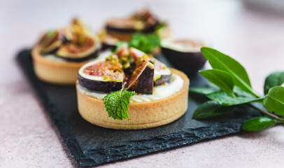 Tartlets pastry with white cream, topped with figs and pistachio, pink background. Cooking concept. Healthy dessert.