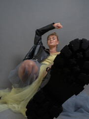 Fashionable blonde woman in black eco-leather boots, jacket, transparent tulle skirt, studio shot on a gray background, vertical photo, shoes in focus in the foreground