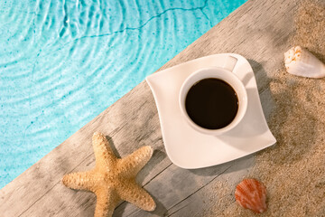 Tasse de café vu du dessus sur un dallage en bois au dessus d'une piscine avec une étoile de mer....