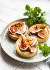 Delicious tartlet with crispy almond-flavored pastry, delicate cheese cream and figs, gray tilled background. Autumn dessert. National Dessert Day, October 14.