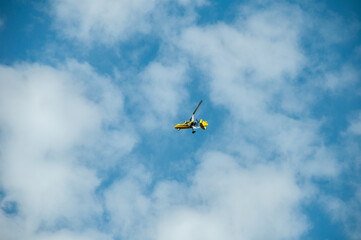 Fototapeta na wymiar A yellow motorized hang glider with a propeller soars in the blue sky against the background of clouds