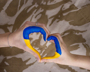 female and child's hand folded in the shape of a heart on a camouflage background. Family, patriotism, unity, support. Russia's invasion of Ukraine, call to world community for help to Ukrainians