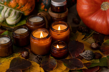 Soy candles burn in glass jars. Tree leaves, pumpkin. Comfort at home. Candle in a brown jar. Scent and light. Scented handmade candle. Aroma therapy. Autumn mood. Cozy home decor in fall.