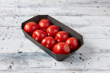 A box of red ripe tomatoes in a cardboard box on a white wooden background