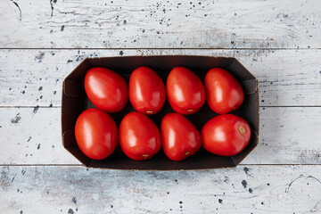 A box of red ripe tomatoes in a cardboard box on a white wooden background, top view