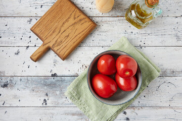 Fresh tomatoes in a plate on a white wooden background, top view
