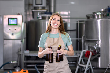 Portrait of female brewer in craft brewery holding a beer bottle.