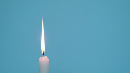 A single wax candle burning on a blue background
