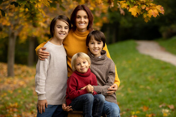 Fototapeta premium Cute blond toddler child and sibling brothers, standing next to autumn wooden stand with decoration, apples, leaves, mug, hedgehock in the park
