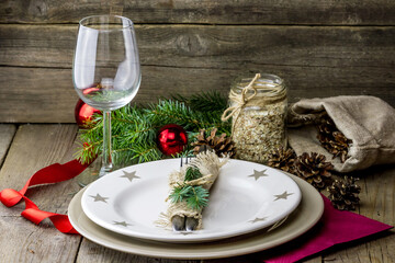 Christmas (New Year) dinner composition. Silver fork and knife decorated fur-tree branches on the plate, wine glass, red curly ribbon with glass balls and cones on wooden background