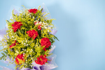 Obraz na płótnie Canvas flower bouquet of red carnation with green leaves on blue background