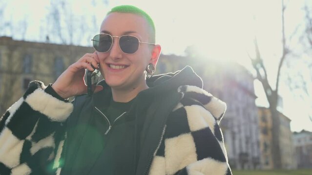 Curvy young androgynous having a phone call with friends, female person using smart phone outdoor
