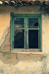 Weathered yellow plaster wall with a neglected green wooden window with broken glass.