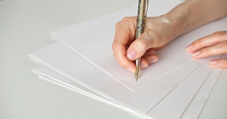 A woman writes with a pen on a white blank sheet of paper. Close up