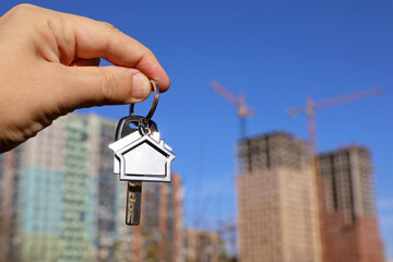 Real estate agent, keychain in shape of a house and key in male hand on background of construction cranes and new buildings. Byung apartment or renting property