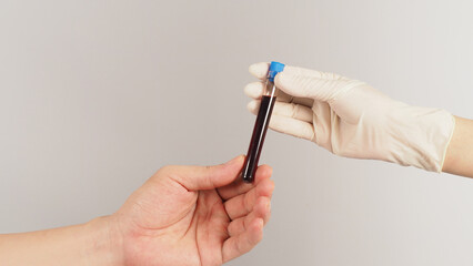Two hands send and receive a blood test tube on white background. One hand wear latex glove.