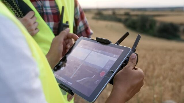 Tablet screen and remote controller drone flying app operated by engineers surveying wind electricity turbines. Aerial technology for maintenance work 