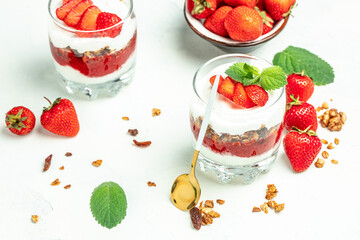 strawberry parfaits with fresh fruit, yogurt and granola on white table, glass jar. Healthy breakfast. Long banner format. top view