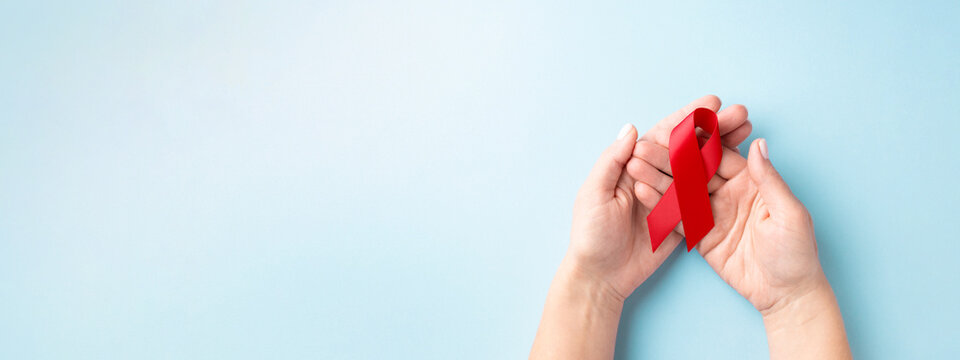 World AIDS Day banner with hands holding red ribbon on blue background.