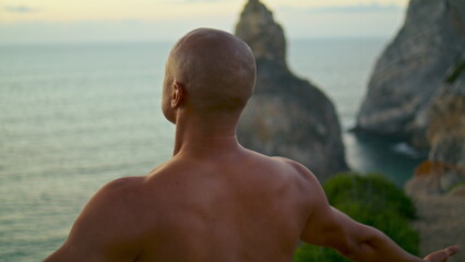Calm yogi meditating ocean cliff closeup. Muscular athletic back at sunset sea